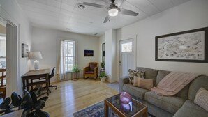 Un salon spacieux doté d’un ventilateur de plafond, d’une grande fenêtre, d’un canapé, d’une table basse et d’une carte accrochée au mur.