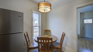 Une cuisine équipée d’un réfrigérateur en acier inoxydable, d’une table à manger en bois avec quatre chaises et d’un luminaire suspendu.