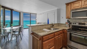 A modern kitchen with granite countertops, wooden cabinets, a stainless steel sink, and a built-in oven. - Sleek Oceanfront King Suite! Dogs OK (Myrtle Beach)
