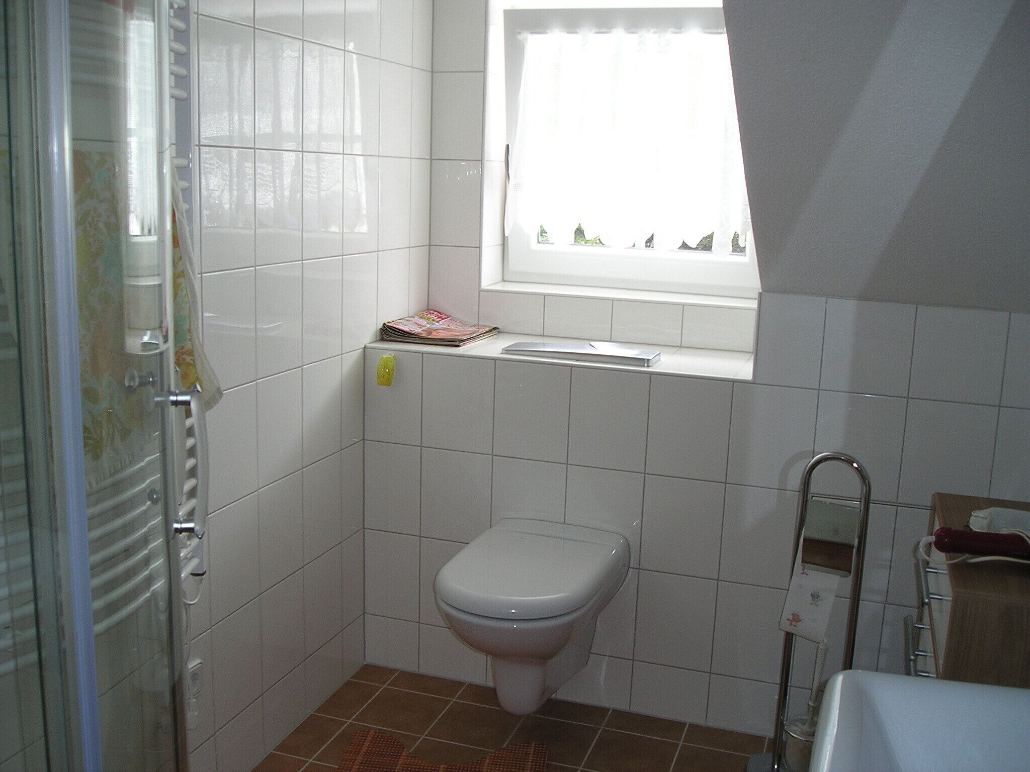 Ein kleines Badezimmer mit Fliesen, einer Toilette, einem Fenster und einer Duschkabine.