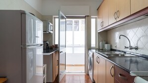 Een kleine keuken met een koelkast, magnetron, spoelbak en wasmachine.