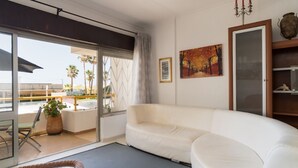 Een moderne woonkamer met een witte bank, een glazen deur die uitkomt op een balkon en een schilderij aan de muur.
