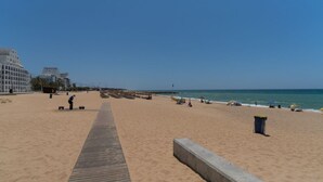 Een strand met een houten looppad, zandstrand en gebouwen op de achtergrond.