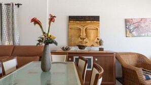 Een eetruimte met een glazen tafel, stoelen, een vaas met bloemen, een Boeddha-schilderij en een rieten stoel.