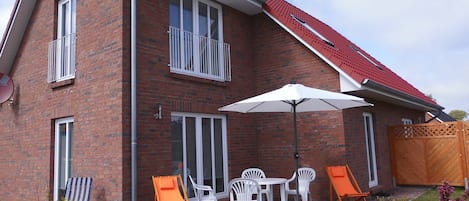 A two-story brick house with a red roof, a patio with outdoor furniture, and a wooden gate.