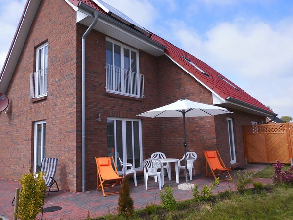 A two-story brick house with a red roof, a patio with outdoor furniture, and a wooden gate.