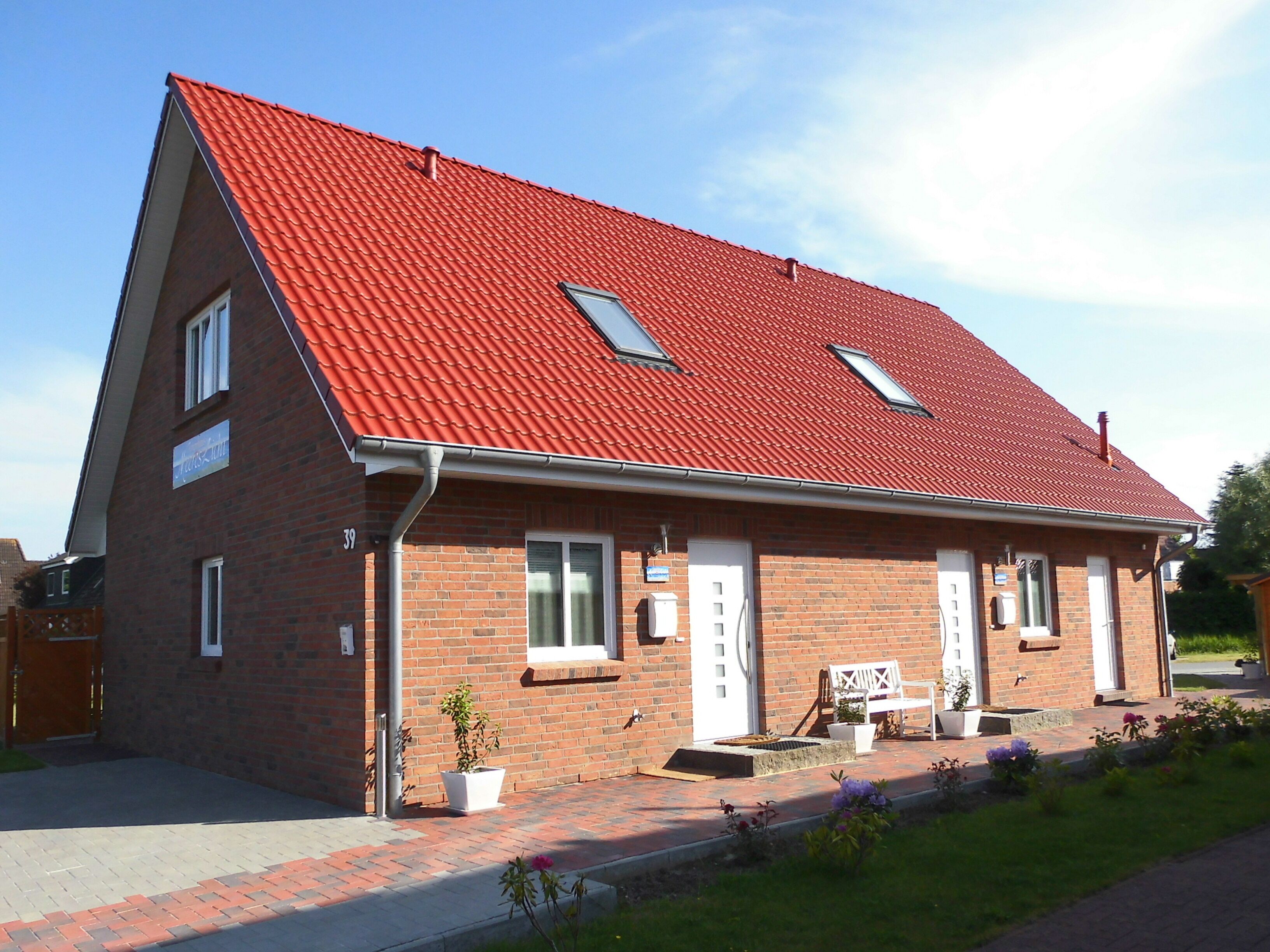 A two-story brick building with a red-tiled roof, a small porch with a bench, and a signboard.