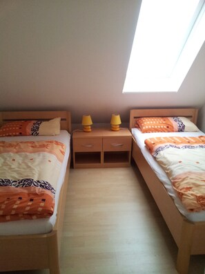 Una habitación pequeña y bien iluminada con dos camas individuales, cada una con ropa de cama estampada y una mesita de noche con dos lámparas.
