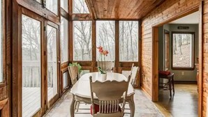 A wooden cabin interior with a dining table and chairs, large windows, and a view of the surrounding forest. - Lake Arrowhead GA Modern Rustic Private Mountain Cabin Chalet Home (Waleska)