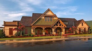 A large, two-story house with a prominent front porch, stone foundation, and a sloped roof. - Lake Arrowhead GA Modern Rustic Private Mountain Cabin Chalet Home (Waleska)
