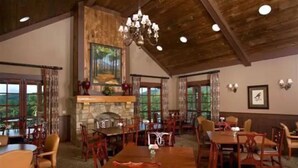 A spacious dining area with high ceilings, wooden beams, and a stone fireplace. Tables and chairs are arranged for dining. - Lake Arrowhead GA Modern Rustic Private Mountain Cabin Chalet Home (Waleska)