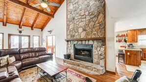 A spacious living room with a stone fireplace, leather sofa, and a wooden ceiling. - Lake Arrowhead GA Modern Rustic Private Mountain Cabin Chalet Home (Waleska)