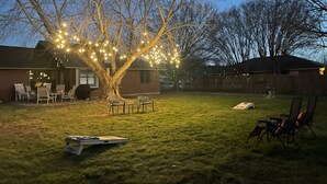 Un jardin avec un arbre décoré de guirlandes lumineuses, un barbecue et du mobilier d’extérieur.