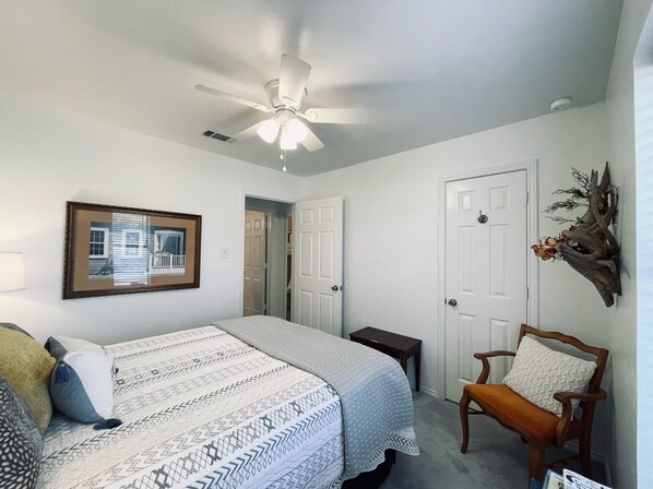 Una camera da letto con un letto, una sedia, una ventola a soffitto, un quadro incorniciato e una porta.