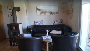 A cozy living room with a black leather sofa, two armchairs, a small wooden table, and a fireplace. - Fantastic FH, terrace, fireplace, close to the Baltic Sea, Bodden view (Fuhlendorf)