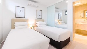 A hotel room with two beds, a large mirror, a bathroom with a sink, and framed artwork on the walls. - Oceanside Apartment with Bay Views (Batemans Bay)