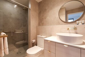 Un baño con ducha de mampara, inodoro y tocador con lavabo y espejo.