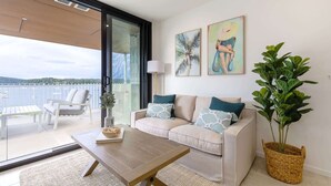 A modern living room with a sofa, a coffee table, and a large potted plant. - Oceanside Apartment with Bay Views (Batemans Bay)