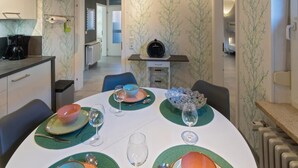 A dining area with a round table set for four, a coffee machine, and a view into a hallway. - Vacation apartment Möwenblick (Norden)