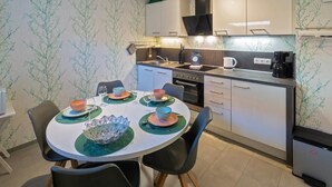 A modern kitchen with a round dining table, black chairs, and a coffee machine. - Vacation apartment Möwenblick (Norden)