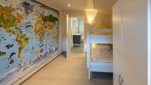 A hallway with a world map mural, bunk beds, and a bathroom visible through an open door. - Vacation apartment Möwenblick (Norden)