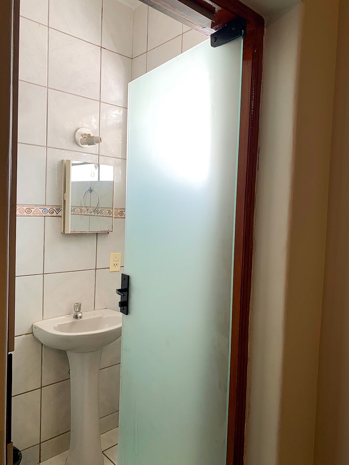 A bathroom with a white sink, a mirror, and a frosted glass door.