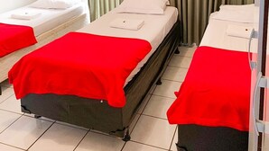 A hotel room with two single beds, each with a red blanket and white pillows. The room has a large window with green curtains, a white wall, and a tiled floor. - HOTEL CENTRAL BARAO DO RIO BRANCO  (Anapolis)