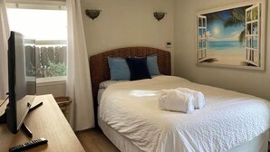 Habitación de hotel con cama, escritorio con control remoto, ventana con cortinas e imagen colgada en la pared.