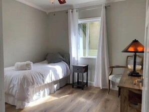 Un dormitorio con cama, mesita de noche, lámpara y ventana con cortinas.