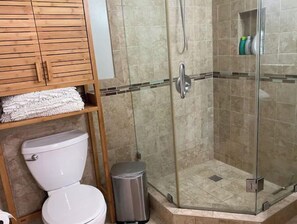 Un baño con inodoro, ducha con mampara de vidrio y un armario de madera con toallas.