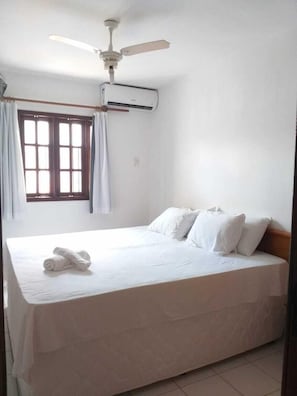 Una cama individual con ropa de cama blanca, un ventilador de techo y un equipo de aire acondicionado en la pared.