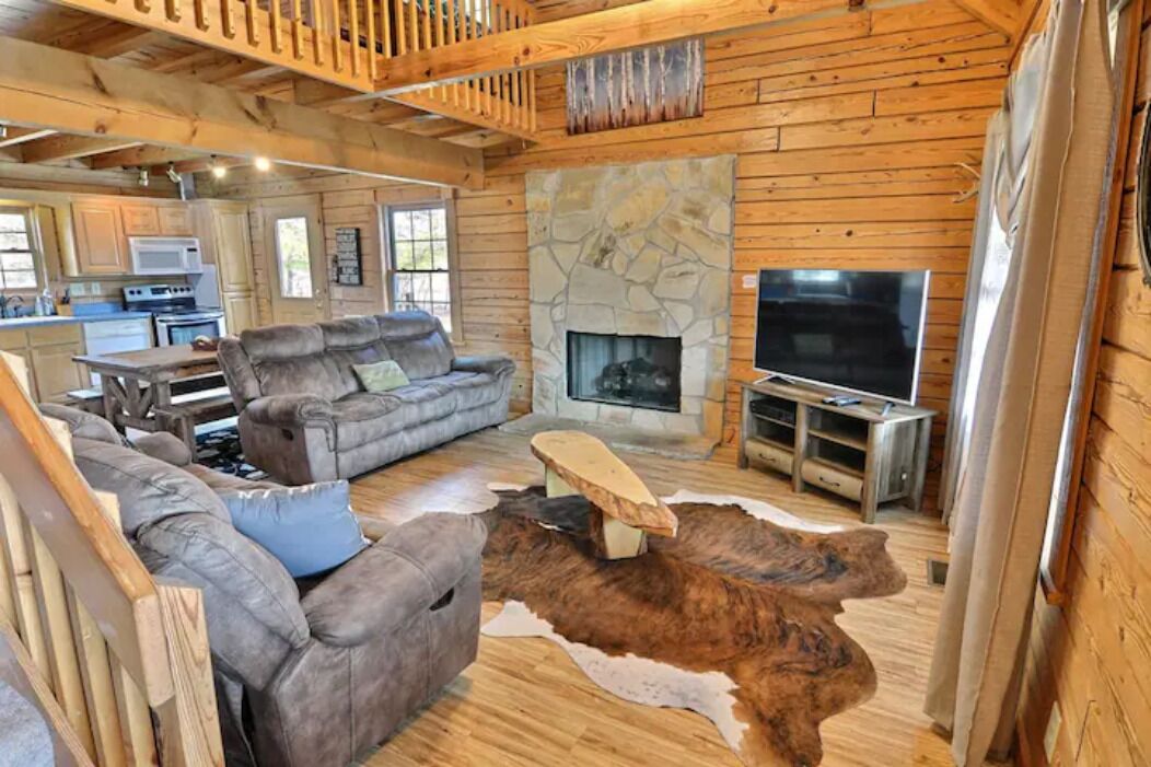 A log cabin interior with a stone fireplace, a television, and a sofa.