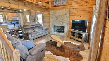 A log cabin interior with a stone fireplace, a television, and a sofa.