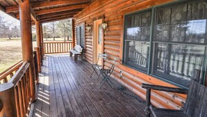 Uma cabana de tronco com um deck de madeira, um banco e uma janela com moldura decorativa.