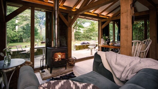 A cozy cabin interior with a wood-burning stove, a sofa, and a dining table.