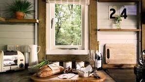 A rustic kitchen with a wooden countertop, a loaf of bread, a bottle of wine, and a window with a view of trees.