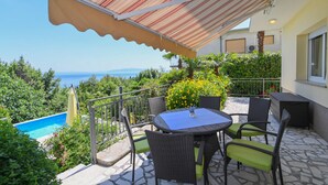 A patio with a table and chairs, a pool, and a view of the sea. - APARTMENTS GROZIC **** OPATIJA - APARTMENT A2 (Opatija)