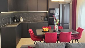 A modern kitchen with dark cabinets, a marble backsplash, and a dining area with red chairs and a grey sofa. - APARTMENTS GROZIC **** OPATIJA - APARTMENT A2 (Opatija)