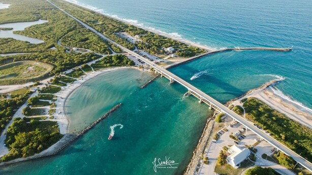 Vista aerea di una zona costiera con un ponte, acque turchesi cristalline e vegetazione.