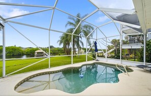 A swimming pool with a glass enclosure, surrounded by a lawn and palm trees.