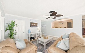 A living room with a ceiling fan, a television, a white entertainment unit, and a dining area visible through an archway.