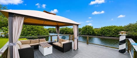 A covered outdoor deck with seating and a view of a body of water.