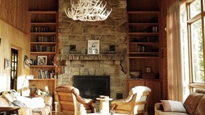 Una sala de estar acogedora con chimenea de piedra, estanterías de madera, mobiliario de cuero y una lámpara de araña original con cuernos.