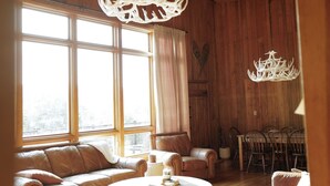 Un salón amplio con techo alto, vigas de madera, ventanas grandes y chimenea.