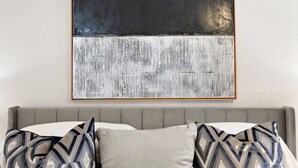 A room with a grey sofa, patterned pillows, and a large abstract painting on the wall.