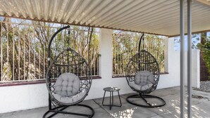 Two hanging chairs under a covered patio with a view of bamboo trees.