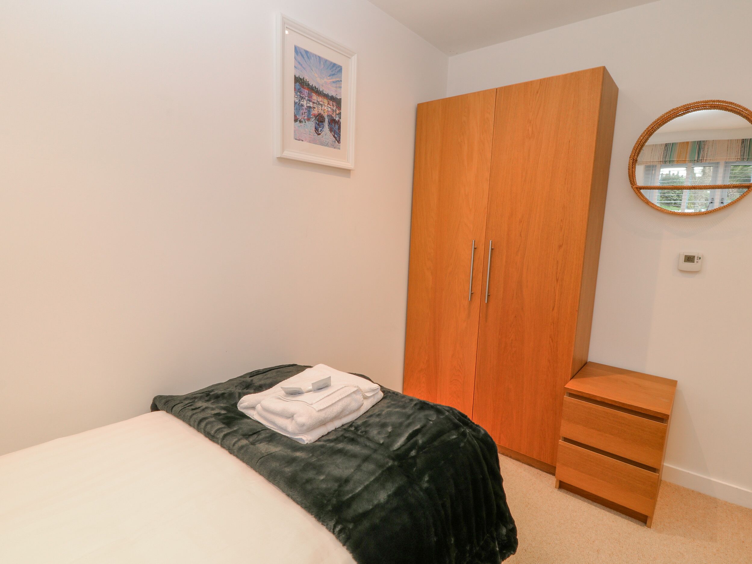 A bedroom with a bed, a wooden wardrobe, a dresser, a mirror, and a framed picture on the wall.