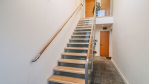 A staircase with wooden steps and a glass railing, leading to a landing with a wooden door and a plant. - A Stone's Throw (Torpoint)