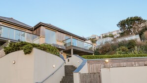 A modern residential building with a curved staircase leading to a wooden deck. - A Stone's Throw (Torpoint)