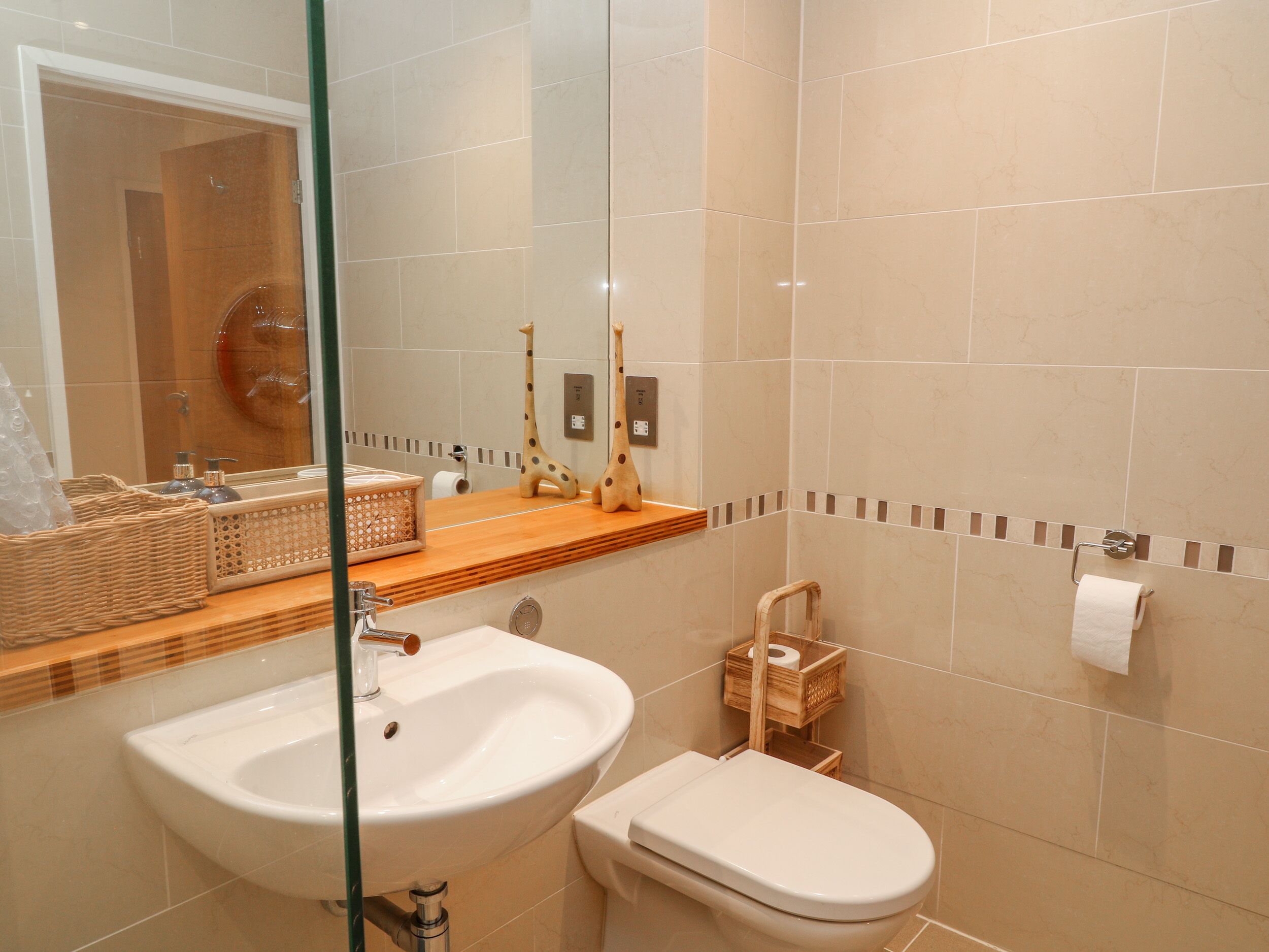 Un baño con un lavamanos grande, inodoro y un espejo sobre el lavamanos. Hay artículos de tocador en la encimera del lavamanos y un perchero en la pared.